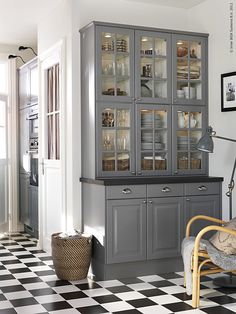 a kitchen with black and white checkered flooring, glass fronted cabinets and chairs