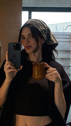 a woman taking a selfie with her cell phone and holding a cup in front of her