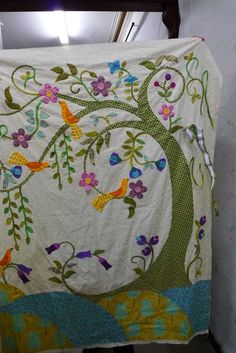 a white blanket with colorful birds and flowers on it hanging from a clothes line in a room