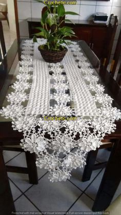 the table is covered with white lace and has a potted plant on top of it