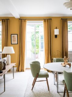 a dining room with yellow walls and green chairs in front of a table that has two lamps on it