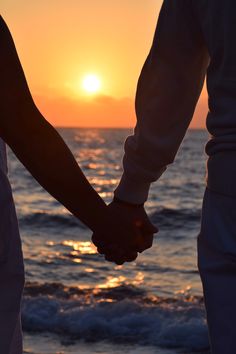 two people holding hands while standing in front of the ocean at sunset or sunrise time