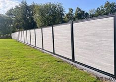 a long fence in the middle of a grassy area with trees and bushes behind it