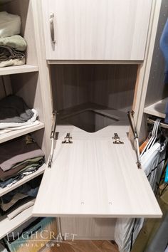 an open closet with clothes on shelves and folded shirts in the bottom drawer, next to a chair