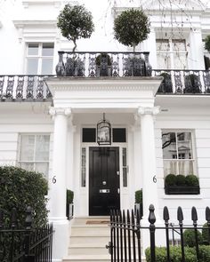 a white house with black wrought iron railings and trees on the balconies