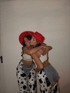 two women hugging each other while wearing cow print pants and red hats on their heads