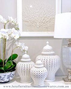 three white vases sitting on top of a table next to a lamp and painting