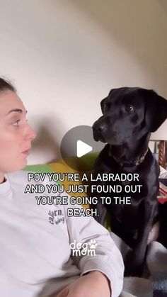 a woman sitting next to a black dog on top of a bed