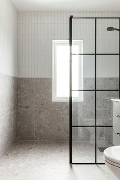 a bathroom with a glass shower door next to a white sink and counter top under a window