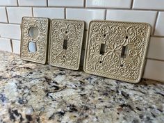 three decorative switch plates sitting on top of a marble counter next to a white tile wall