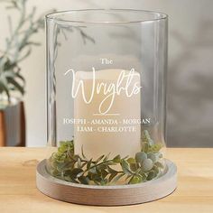 a clear glass candle holder with greenery and the words, the wrights on it