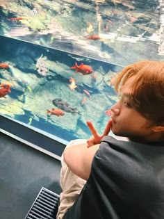 a boy sitting in front of a fish tank with carrots sticking out of his mouth