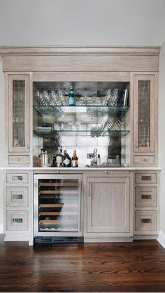 a kitchen with white cupboards and glass shelves filled with bottles, wine glasses and other items