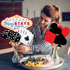 a woman sitting at a table with playing cards and flowers in front of the sign that says, what happens vegas stays in vegas