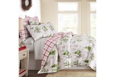 a bed with white and red comforters in front of a window next to a night stand