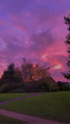 the sky is purple and pink as the sun sets in the distance behind some trees