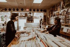 a man and woman standing at a record store counter with records on the shelves in front of them