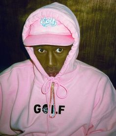 a young man wearing a pink hoodie with the word golf on it and a hat