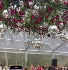 a group of people standing under a white tent with red flowers hanging from it's ceiling