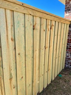 a wooden fence next to a brick wall and green grass in front of the fence