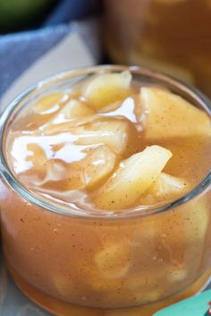 a glass jar filled with apple cider and sliced apples in the background on a table