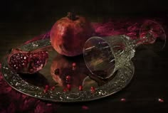 two pomegranates on a glass plate with a wine goblet