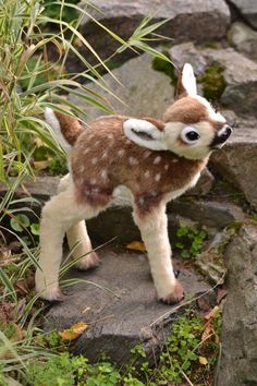 a small stuffed deer standing on top of a rock next to some grass and rocks