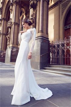 a woman in a white wedding dress standing on the sidewalk near an ornate building with columns