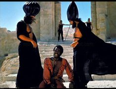 three women dressed in black and orange are sitting on the steps near some stone pillars