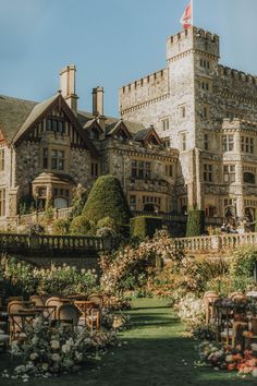 an old castle like building with lots of flowers in the foreground and chairs on the ground