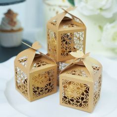 three decorative boxes with tags on them sitting on a white plate next to some cupcakes