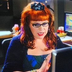 a woman with red hair and glasses is looking at a computer screen