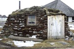 an outhouse made of rocks and grass with a small door in the front yard