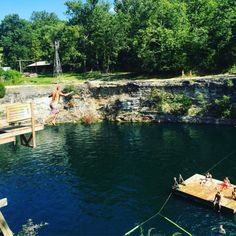 some people are jumping into the water from a dock that is surrounded by rocks and trees