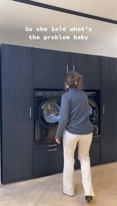 a woman standing in front of a dryer next to a black cabinet with the words so she said what's the problem baby