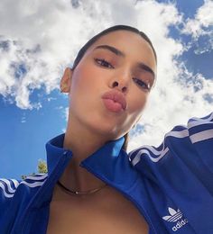 a woman sticking her tongue out in front of the camera with clouds and blue sky behind her