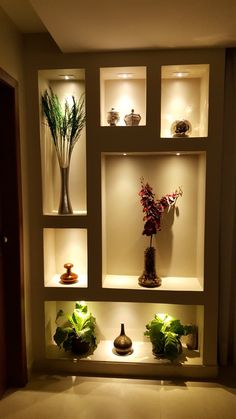 an arrangement of vases and plants on display in a wall niche with lights above them