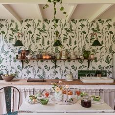 a table with food on it in front of a wallpapered kitchen and dining room