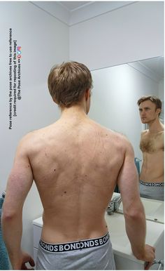 a man with no shirt looking at himself in the mirror