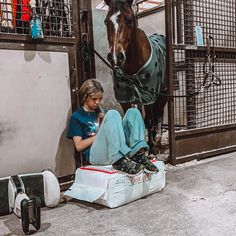 a woman sitting on the ground next to a horse in a stable with its head down