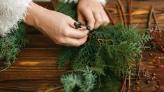 a woman is decorating a christmas wreath with berries and greenery on a wooden table