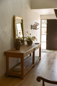 a wooden table with two vases and a mirror on top of it next to a chair