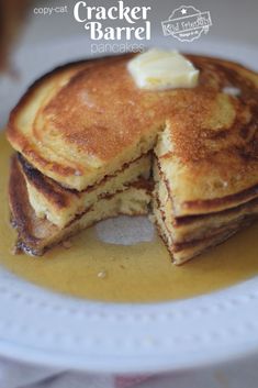 a stack of pancakes on a white plate with a bite taken out of the top