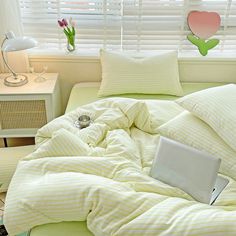 a laptop computer sitting on top of a bed covered in yellow and white striped sheets