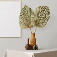 two vases with palm leaves in front of a blank canvas on the wall behind them