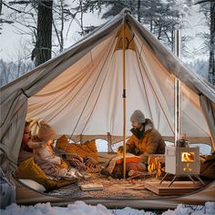 two people sitting in a tent next to each other on snow covered ground near trees