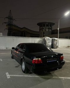 a black car is parked in a parking lot at night with its lights turned on