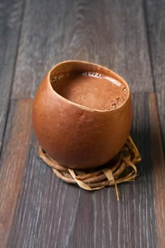 a brown bowl sitting on top of a wooden table next to a cup filled with liquid