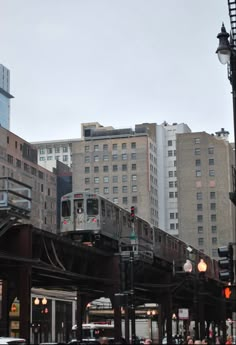 a train traveling over a bridge in the middle of a city with tall buildings behind it