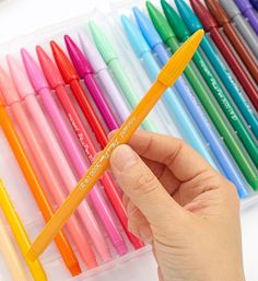 a hand holding a pen in front of many different colored pens